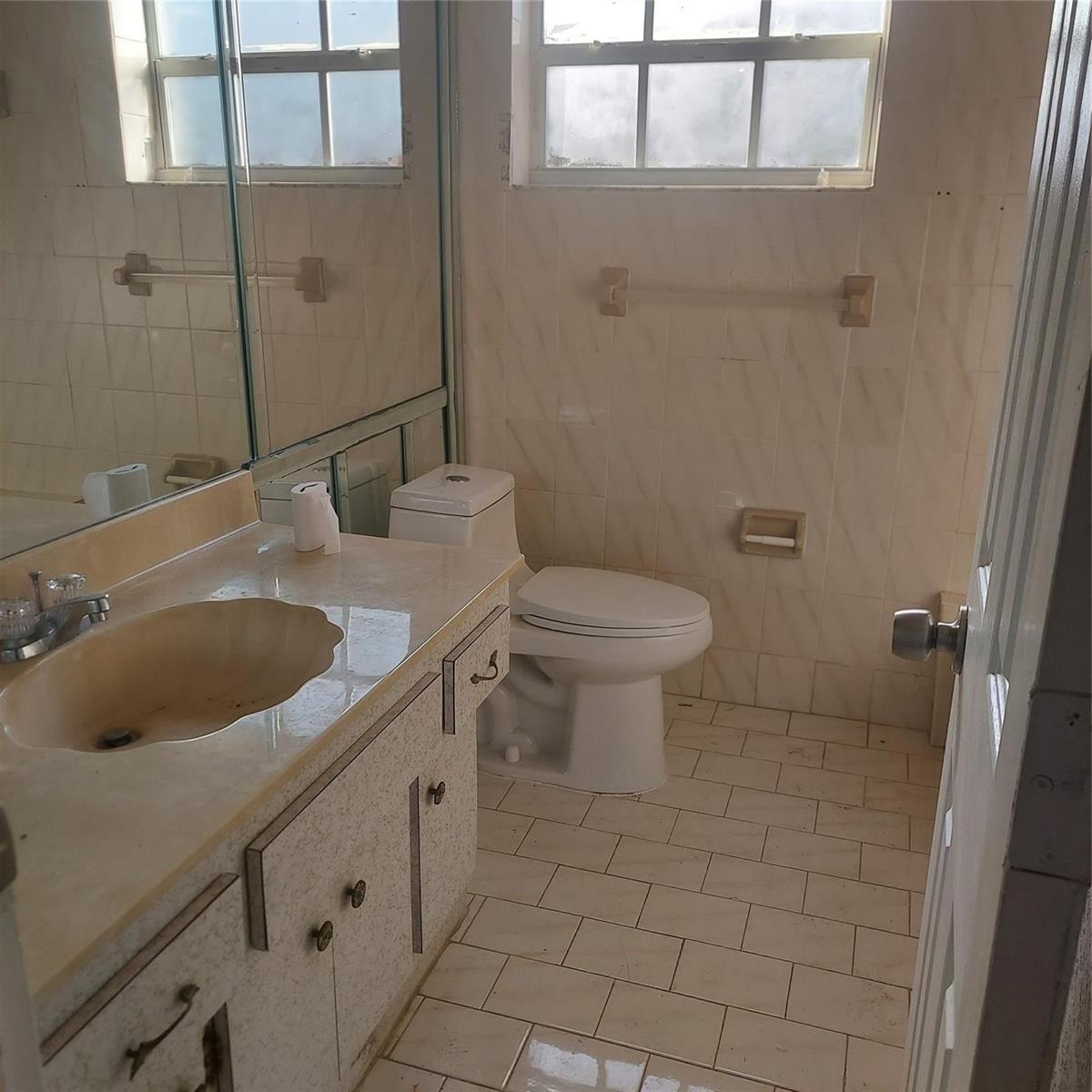 A bathroom with a vanity, toilet, tiled floor, and a large mirror over the sink — LAUDERDALE LAKES, FL