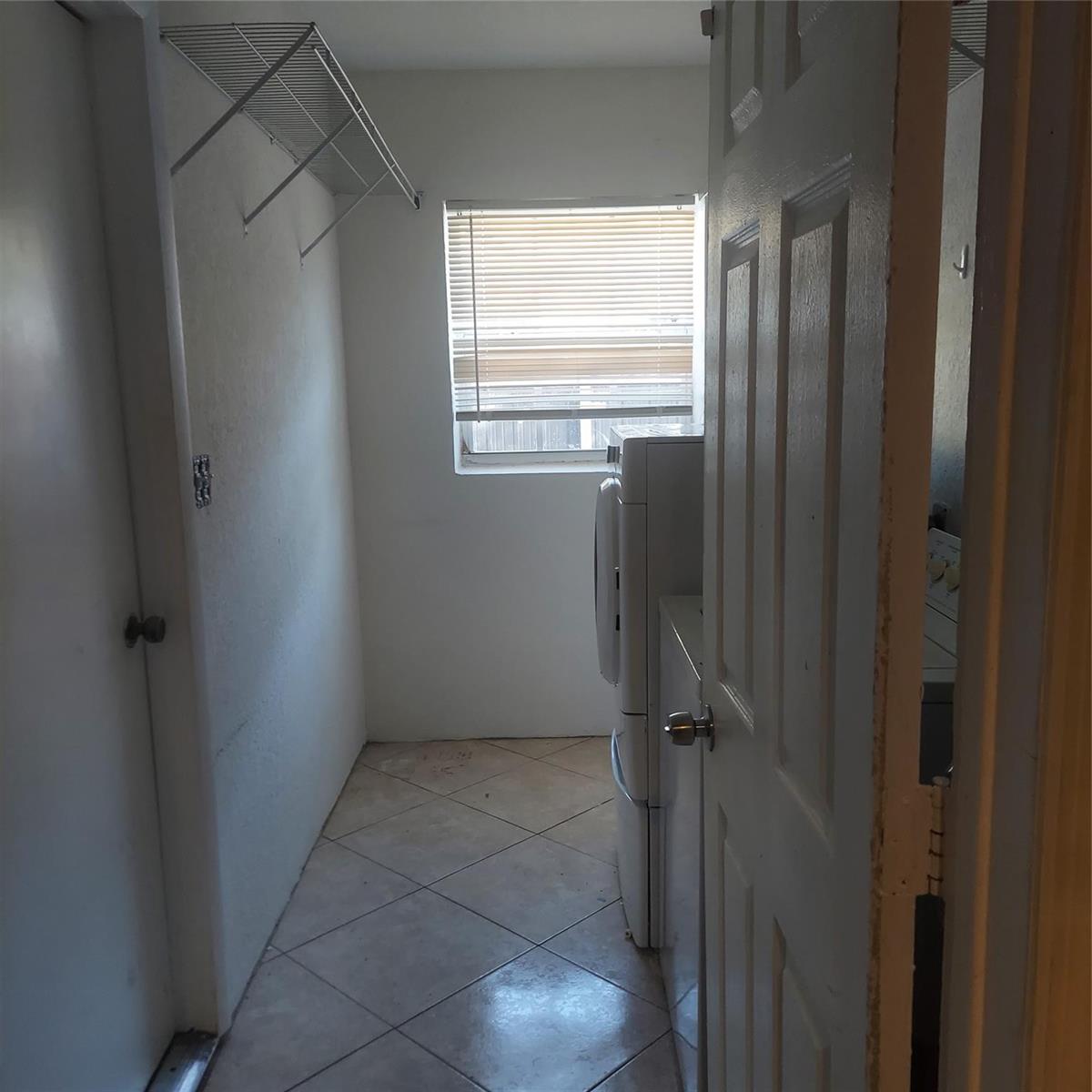A laundry room with tile flooring, a wire shelf, and a window with blinds — LAUDERDALE LAKES, FL