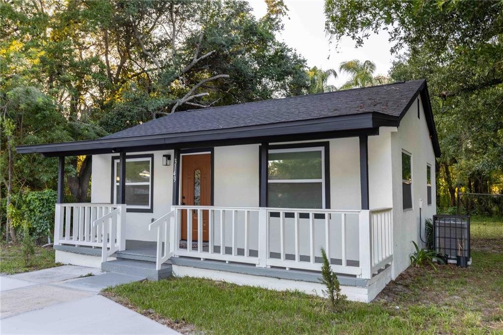 A small, white, single-story house with a dark roof, front porch, and wooden front door — 3149 W WASHINGTON STREET, ORLANDO, FL