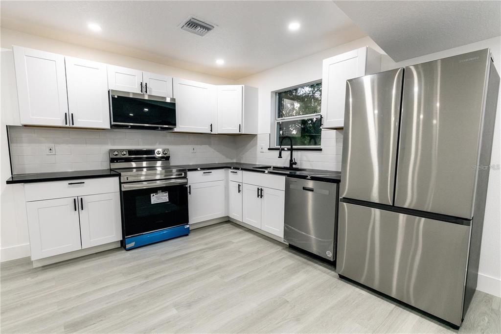 A modern kitchen features white cabinets, stainless steel appliances, black countertops, and light wood flooring — 3149 W WASHINGTON STREET, ORLANDO, FL