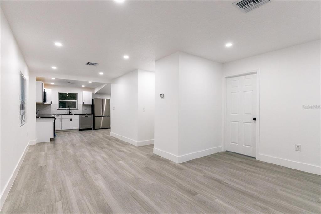 A bright, open-concept room features white walls, light wood-look flooring, and an adjacent kitchen area — 3149 W WASHINGTON STREET, ORLANDO, FL