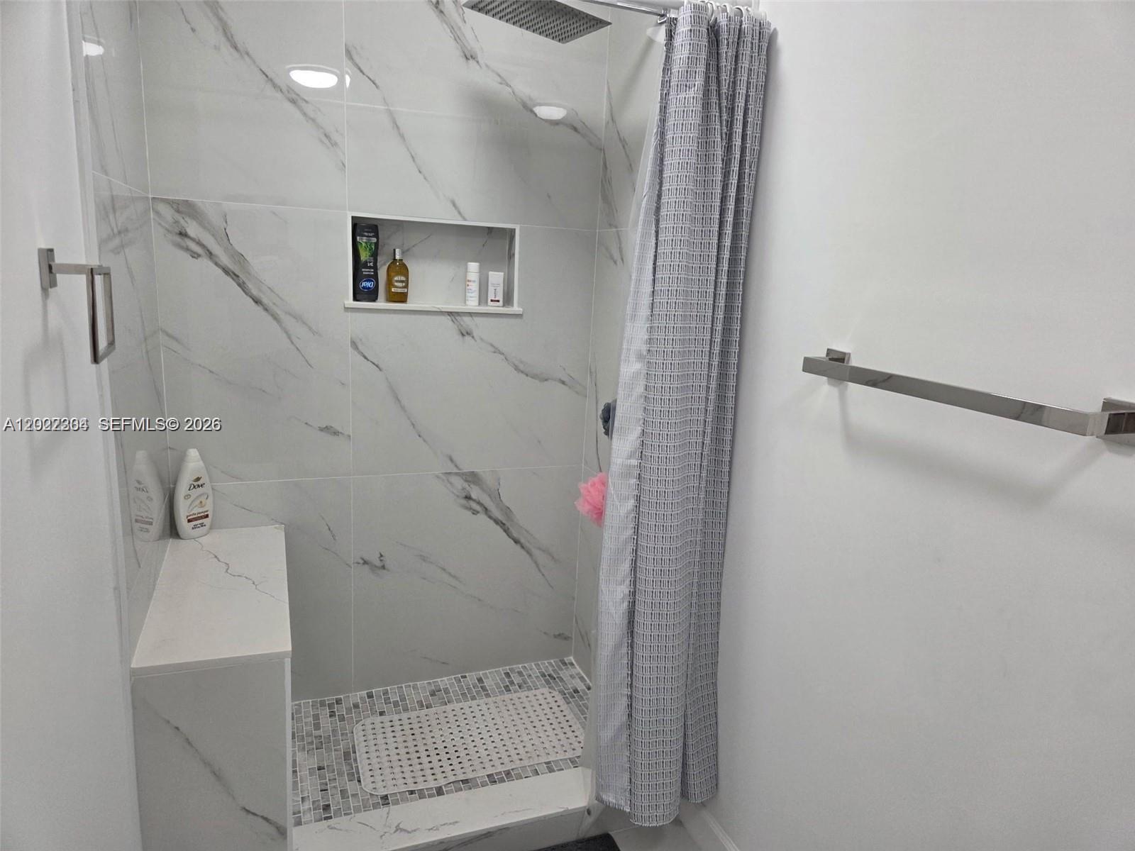 A walk-in shower features marble-look tile walls, a built-in bench, and a patterned shower curtain — 4851 NW 11th Ct, Lauderhill FL 33313, LAUDERHILL, FL