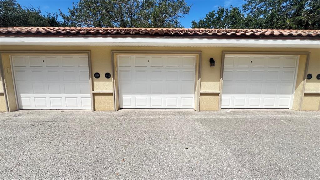 A row of three white garage doors on a tan building with a tiled roof — 75 RIVERVIEW BEND S UNIT 1642, PALM COAST, FL