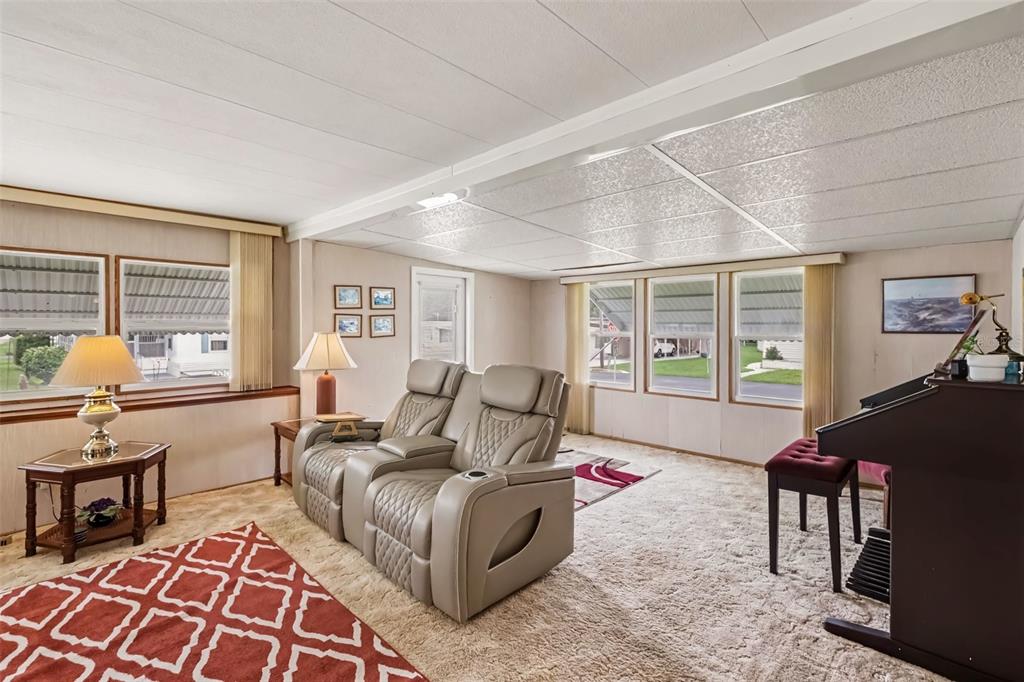 A living room features light-colored carpet, a double recliner, and a piano near large windows — 37249 HAMMOND DRIVE, ZEPHYRHILLS, FL