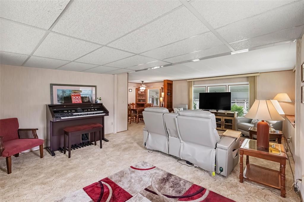 A living room features a piano, a gray reclining sofa, a television, and carpeted flooring — 37249 HAMMOND DRIVE, ZEPHYRHILLS, FL