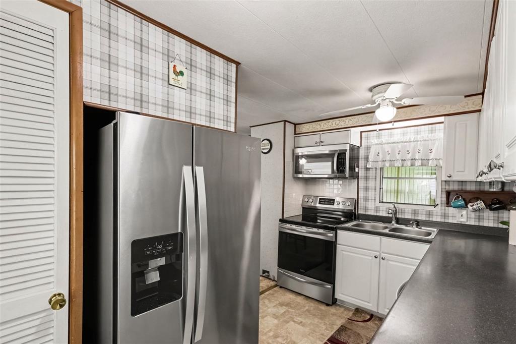 A kitchen features stainless steel appliances, white cabinets, dark countertops, and plaid wallpaper — 37249 HAMMOND DRIVE, ZEPHYRHILLS, FL