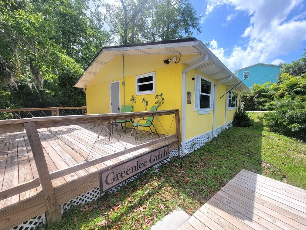 A bright yellow house features a large wooden deck with a sign reading Greenlee Gulch — 7222 TROPICAL DRIVE, WEEKI WACHEE, FL
