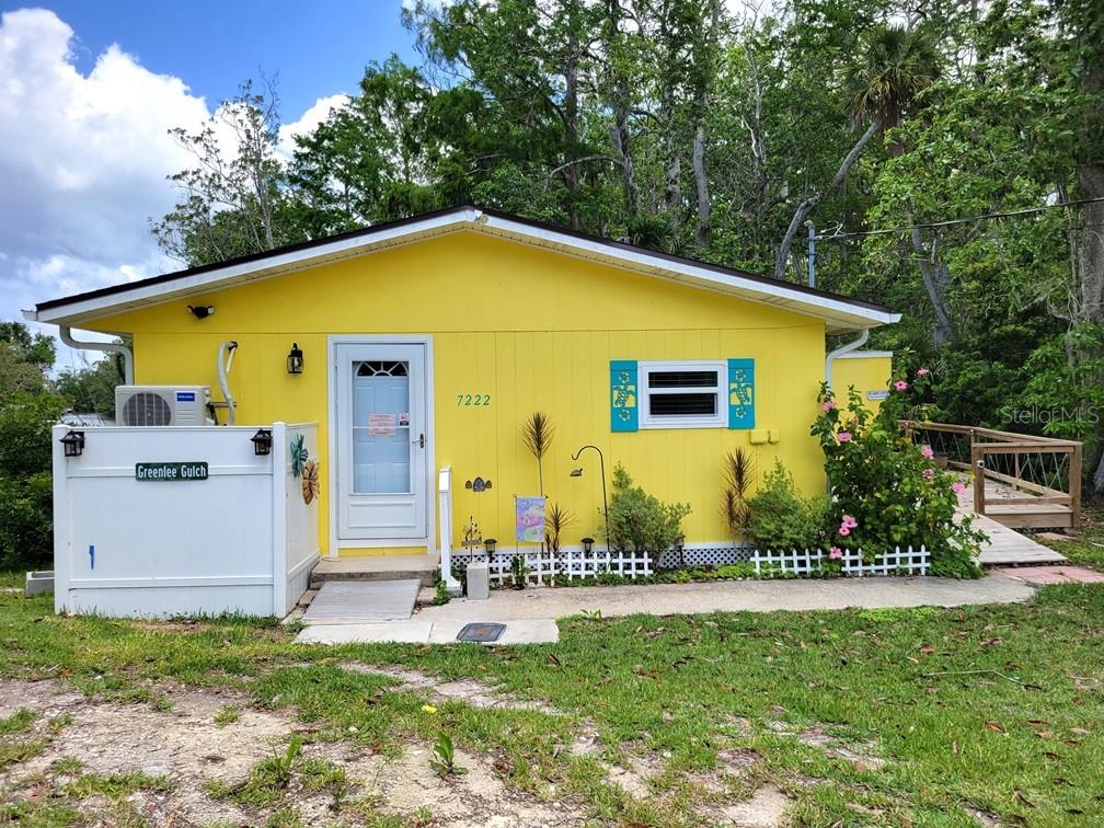 A bright yellow, single-story house features a white door, blue shutters, and a small porch — 7222 TROPICAL DRIVE, WEEKI WACHEE, FL