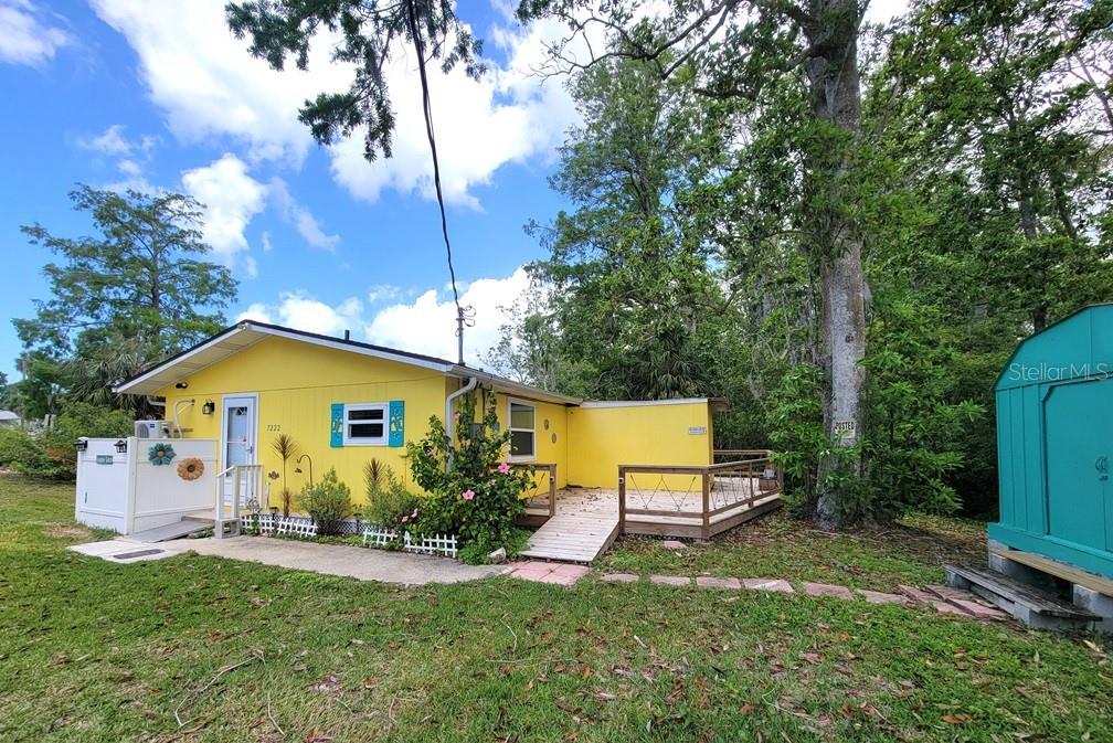 A bright yellow single-story house features a wooden deck, a ramp, and blue shutters — 7222 TROPICAL DRIVE, WEEKI WACHEE, FL