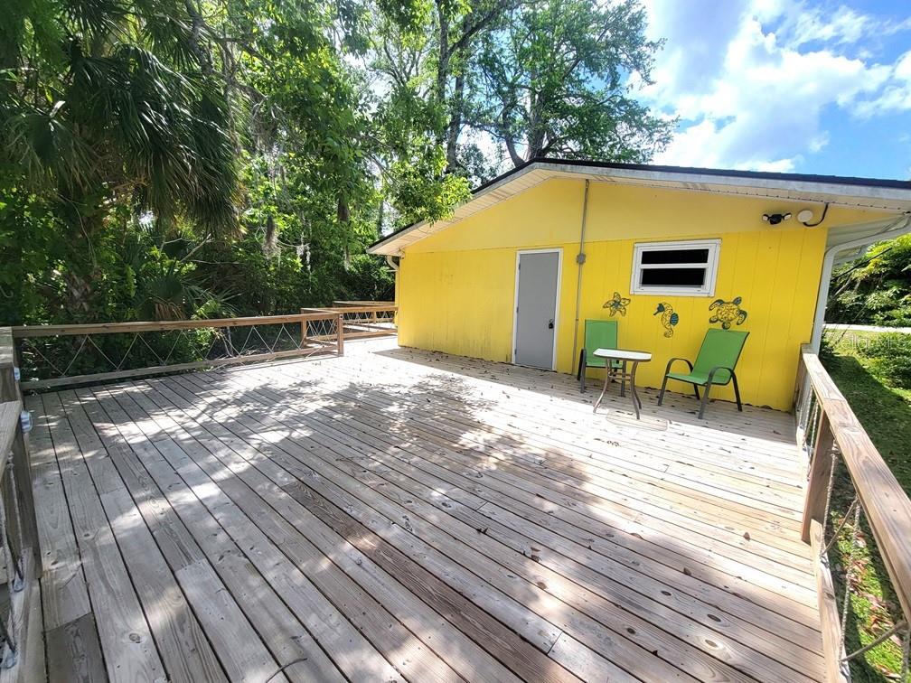 A yellow house with a large wooden deck and two green chairs sits outdoors — 7222 TROPICAL DRIVE, WEEKI WACHEE, FL