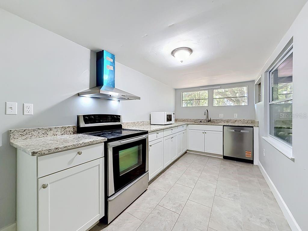 A kitchen features white cabinets, granite countertops, stainless steel appliances, and light-colored tile flooring — 3508 ROUSE ROAD, ORLANDO, FL