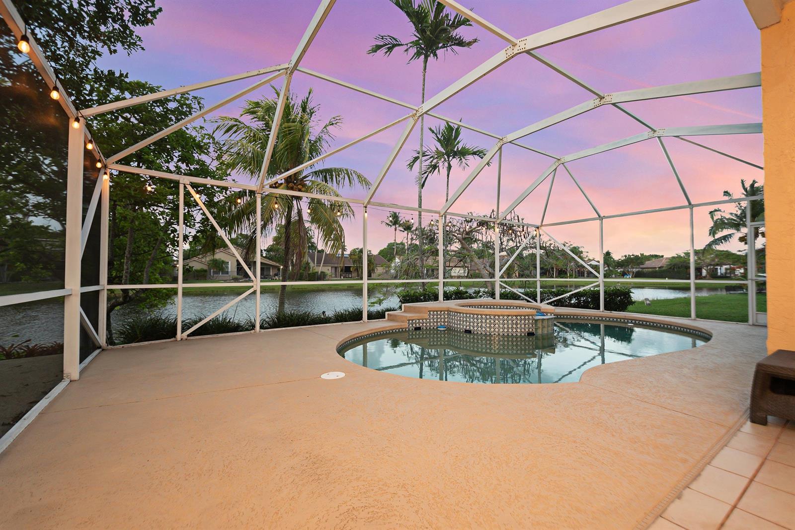 A screened-in pool patio features a built-in spa overlooking a lake at sunset — 412 Cameron Drive, Weston FL 33326, WESTON, FL