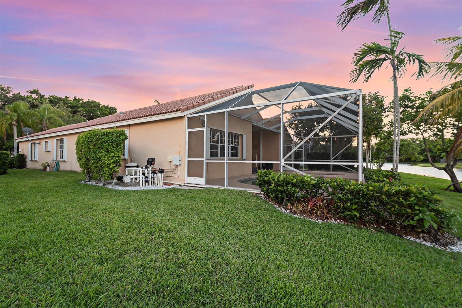 A tan house with a screened-in pool enclosure sits on a grassy lawn at sunset — 412 Cameron Drive, Weston FL 33326, WESTON, FL