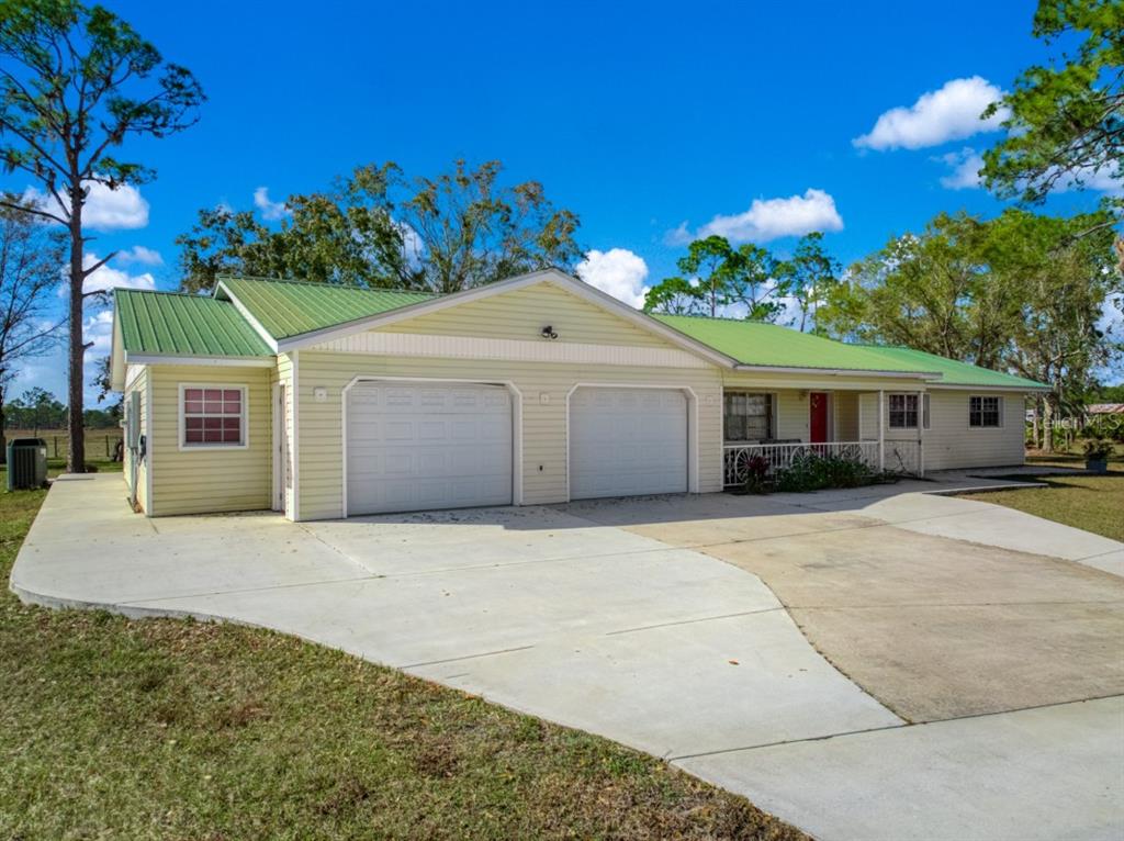 A single-story house with yellow siding, a green metal roof, and a two-car garage — 948 S RIVERDALE ROAD, AVON PARK, FL