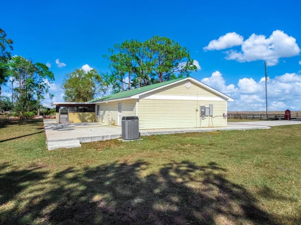 The exterior of a light yellow house with a green roof and a concrete patio — 948 S RIVERDALE ROAD, AVON PARK, FL