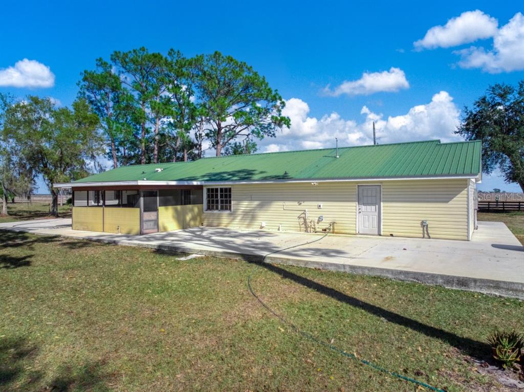 The exterior of a yellow house features a green metal roof and a concrete patio — 948 S RIVERDALE ROAD, AVON PARK, FL