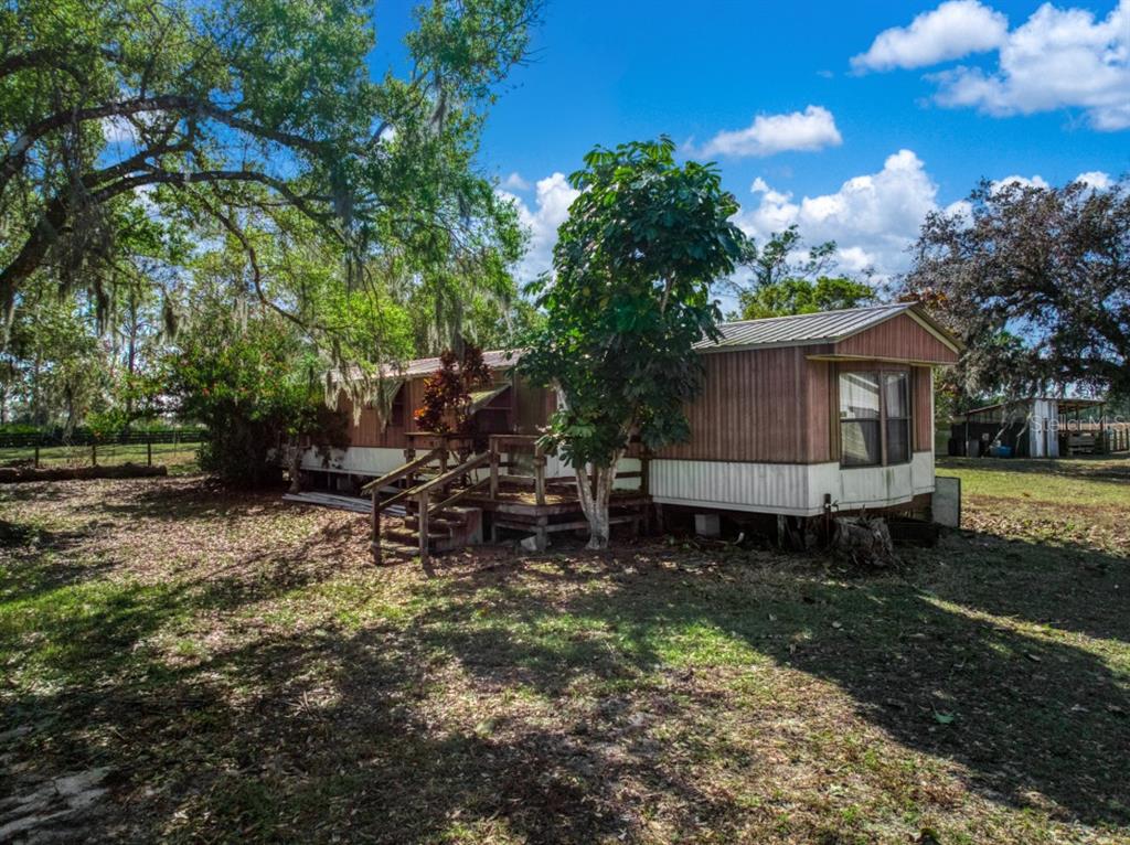 A single-story mobile home with a wooden deck sits on a grassy, tree-shaded lot — 948 S RIVERDALE ROAD, AVON PARK, FL