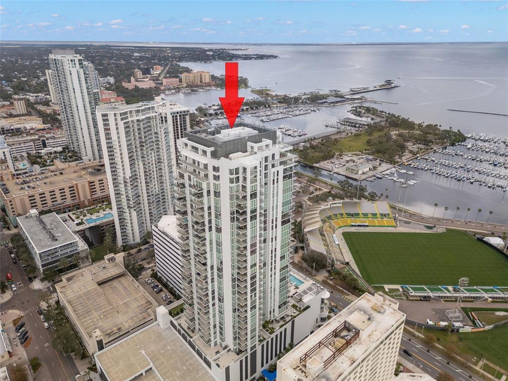 An aerial view shows a tall residential skyscraper with a red arrow pointing to its roof — 301 1ST STREET S UNIT 1204, ST PETERSBURG, FL