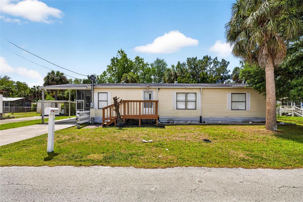 A single-story mobile home with light yellow siding, a wooden front deck, and a carport — 8552 W PEACOCK COURT, HOMOSASSA, FL