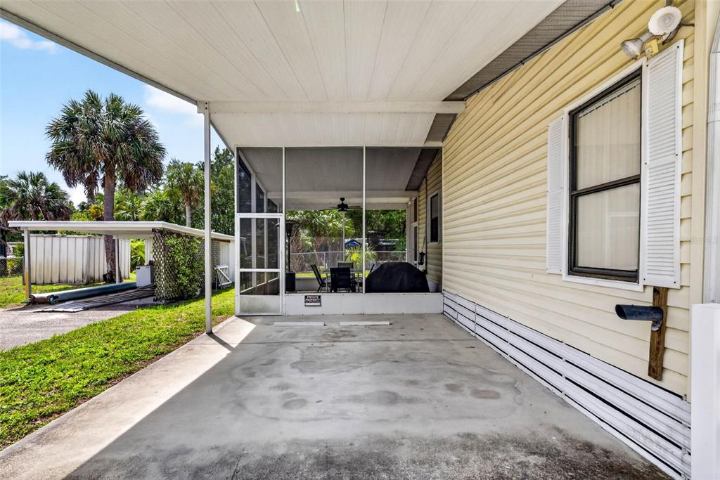 A concrete carport sits beside a screened-in porch and a house with yellow siding — 8552 W PEACOCK COURT, HOMOSASSA, FL