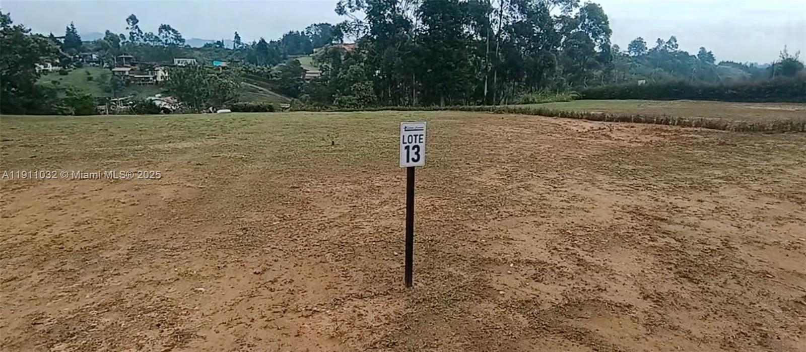 A sign labeled Lote 13 stands in the middle of a large, open dirt lot — Vereda Mampuesto Sector Garrido #13, C Colombia, C