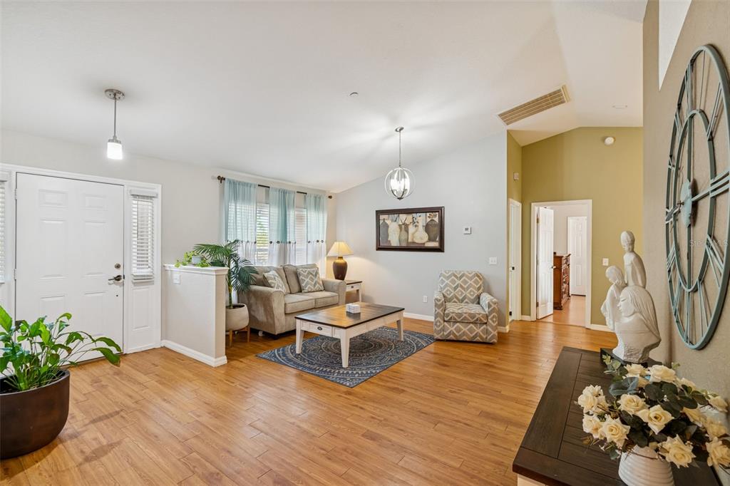 A living room features wood-look flooring, a sofa, an armchair, and a large wall clock — 18030 BAYAMON AVENUE, POLK CITY, FL