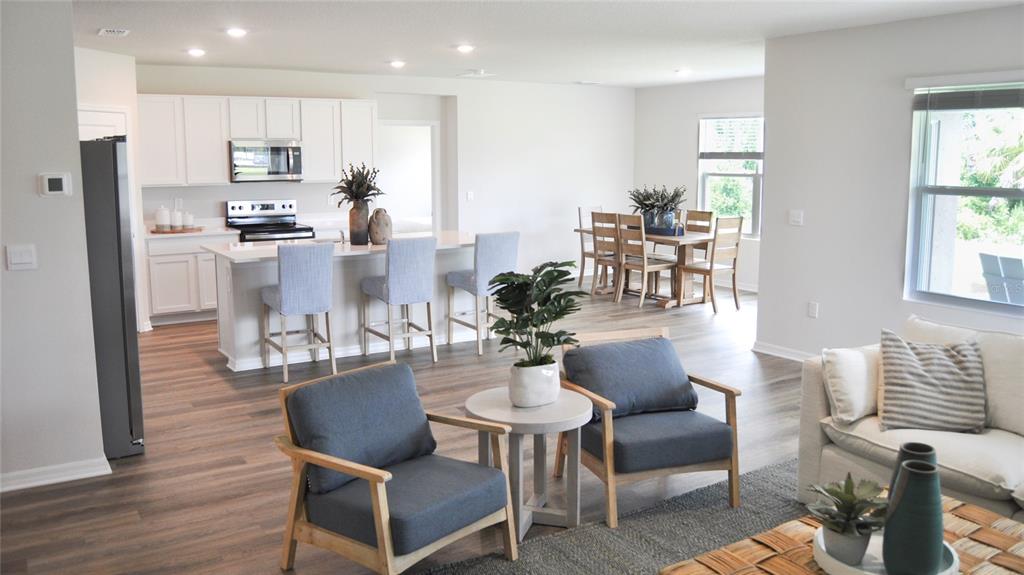 An open-concept kitchen, dining area, and living room feature light wood floors and white cabinetry — 17506 WHISKEY CREEK TRAIL, PARRISH, FL