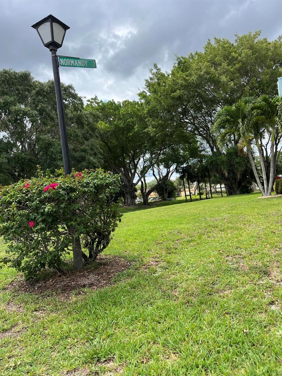 A street sign labeled Normandy stands next to a flowering bush and a grassy lawn — 434 Normandy # J, Delray Beach FL 33484, DELRAY BEACH, FL