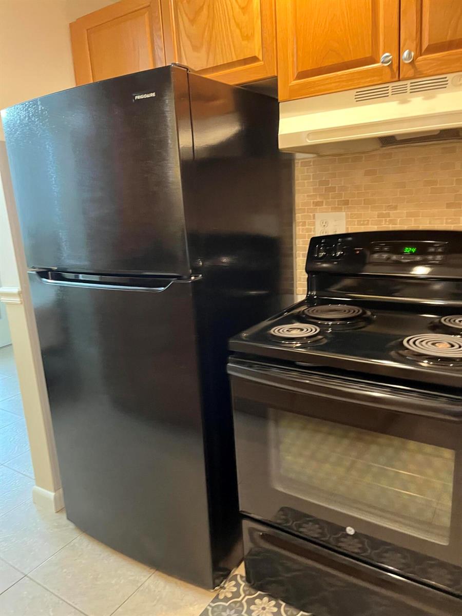 A kitchen features a black refrigerator, a black electric stove, and wooden cabinets — 434 Normandy # J, Delray Beach FL 33484, DELRAY BEACH, FL