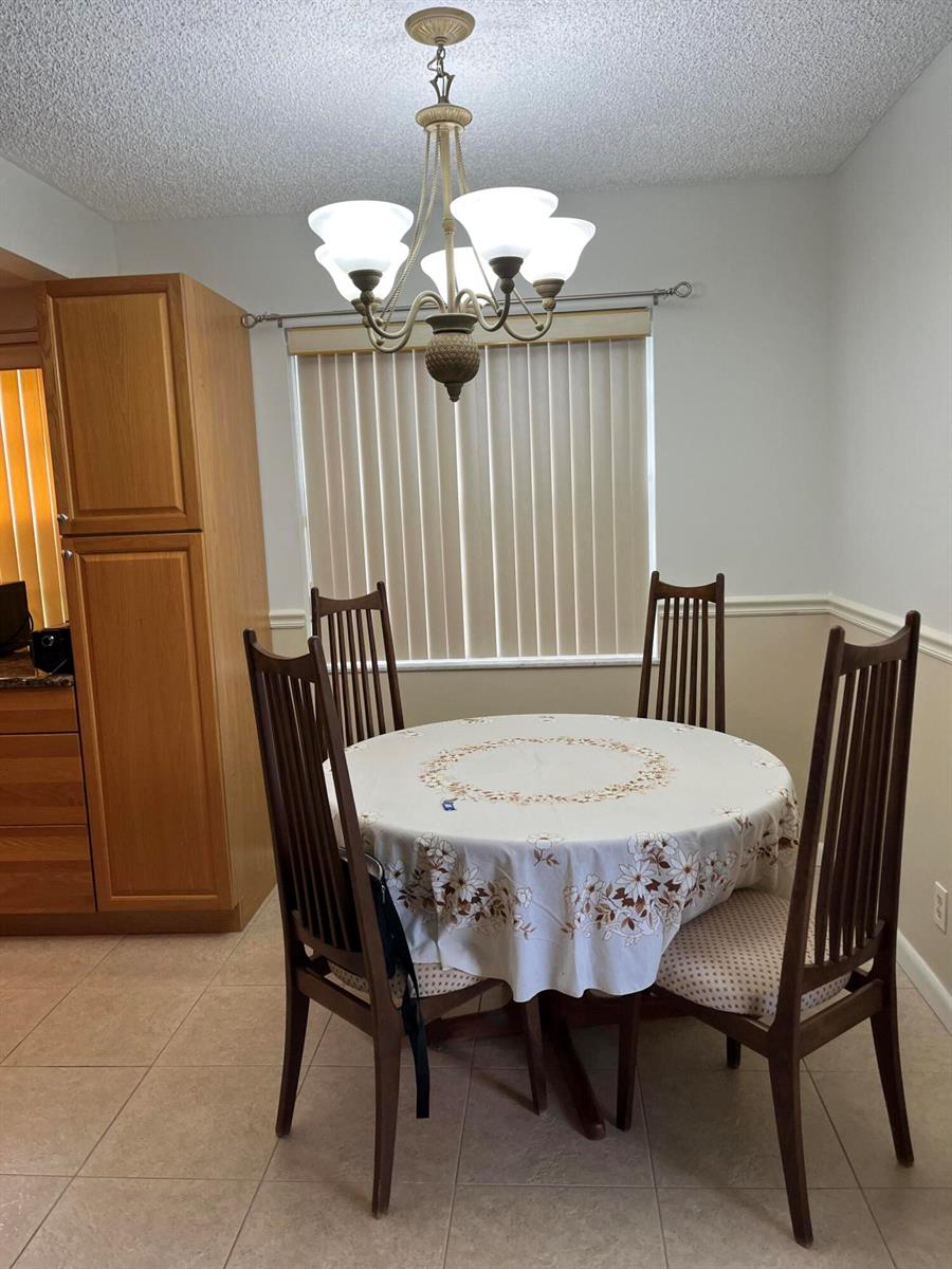 A dining area features a round table with four chairs, a chandelier, and vertical blinds — 434 Normandy # J, Delray Beach FL 33484, DELRAY BEACH, FL