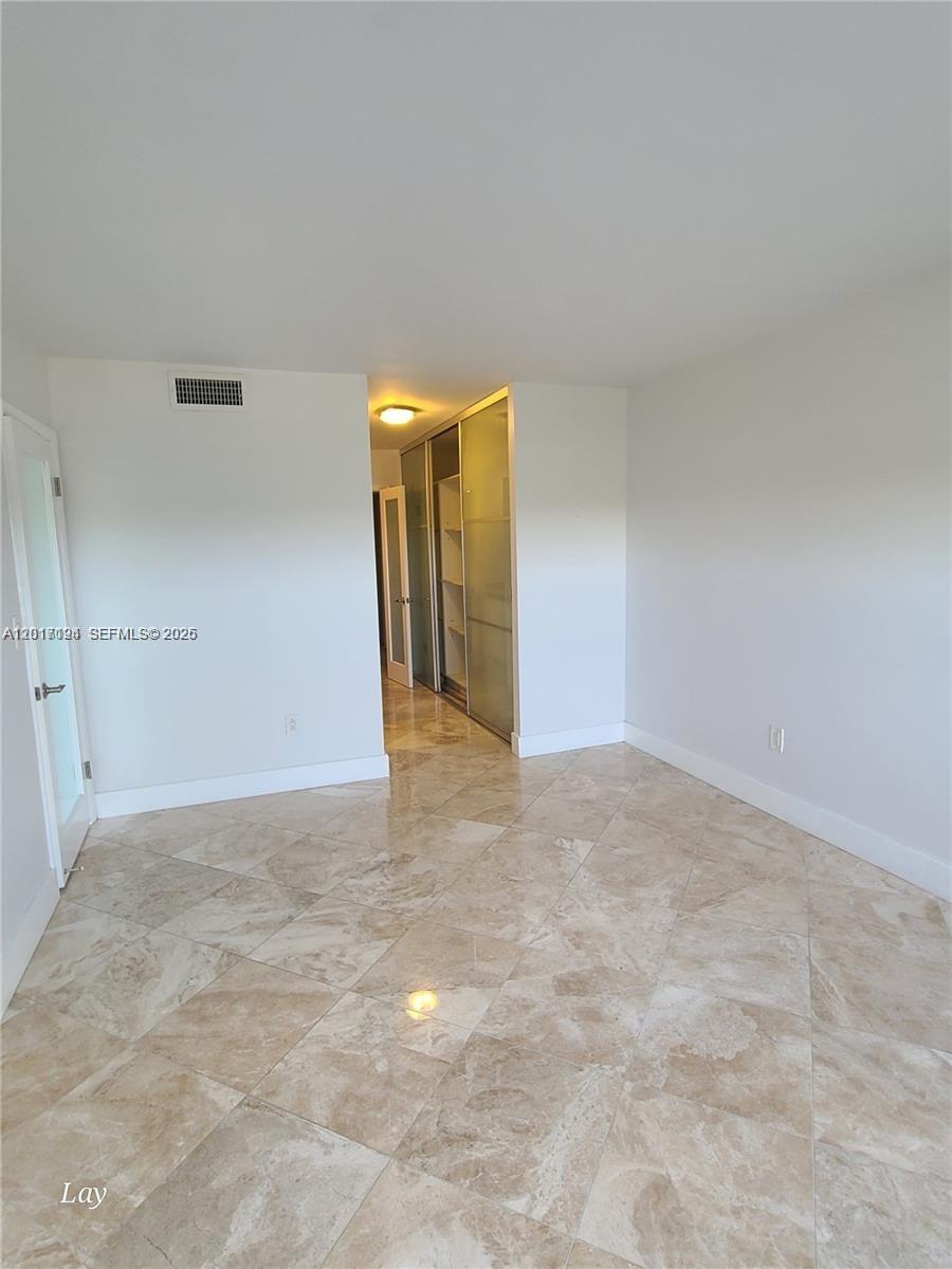 An empty room features beige tile flooring, white walls, and a glass-paneled closet — NORTH MIAMI BEACH, FL