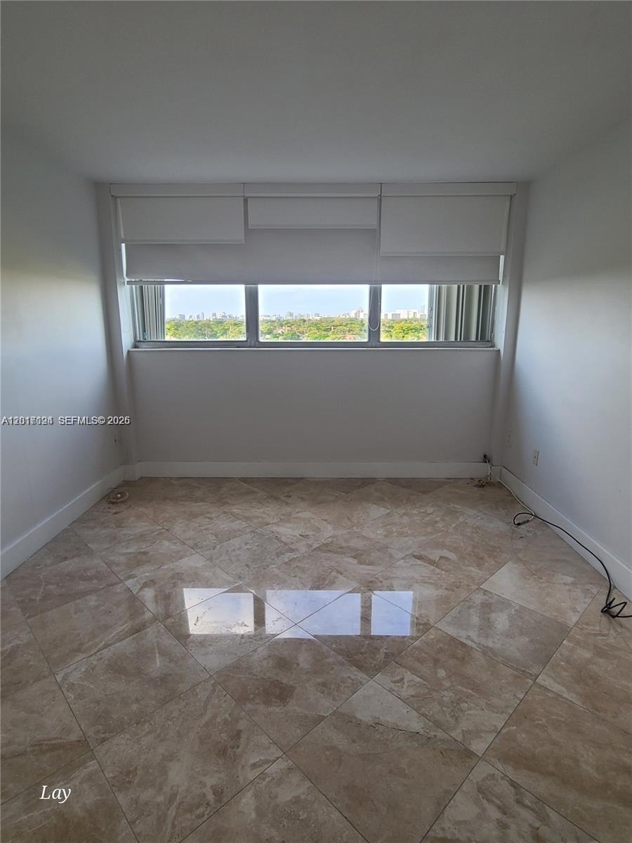 An empty room features beige tile flooring, white walls, and a window with roller shades — NORTH MIAMI BEACH, FL