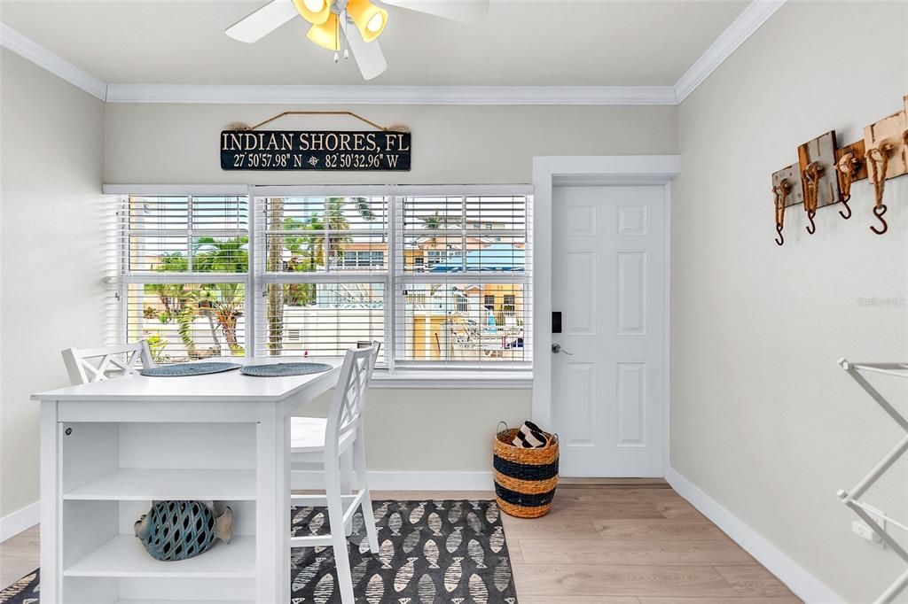 A dining area features a white table, a patterned rug, and a wall sign — 19417 GULF BOULEVARD UNIT A-105, INDIAN SHORES, FL