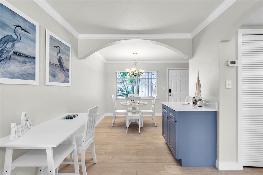 A dining area features a white table, blue kitchen island, and two framed heron prints — 19417 GULF BOULEVARD UNIT A-105, INDIAN SHORES, FL