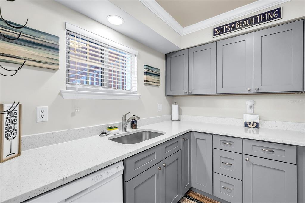 A kitchen features gray cabinets, white countertops, a stainless steel sink, and a window — 19417 GULF BOULEVARD UNIT A-105, INDIAN SHORES, FL