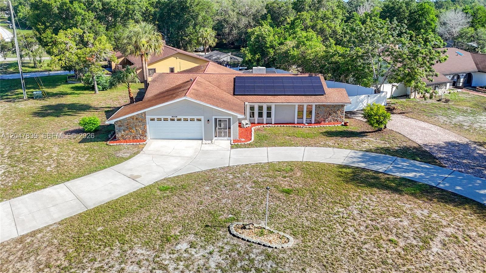 An aerial view shows a single-story house with a solar panel array on the roof — 8209 Chaucer Dr, Spring Hill FL 34607, SPRING HILL, FL