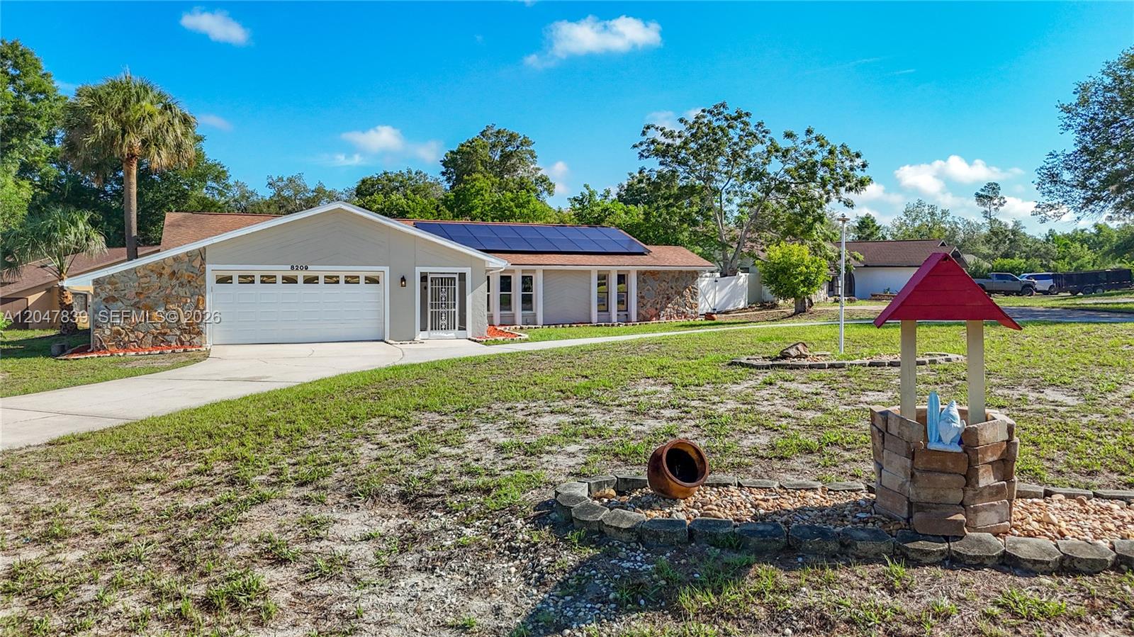 A single-story house with a white garage, solar panels, and a decorative stone well — 8209 Chaucer Dr, Spring Hill FL 34607, SPRING HILL, FL