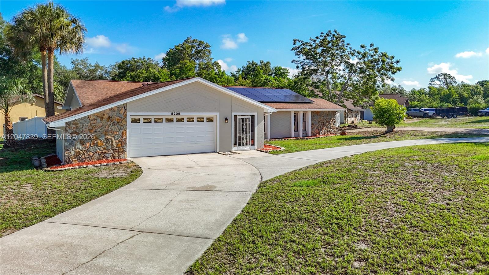 A single-story house features a stone facade, a two-car garage, and rooftop solar panels — 8209 Chaucer Dr, Spring Hill FL 34607, SPRING HILL, FL