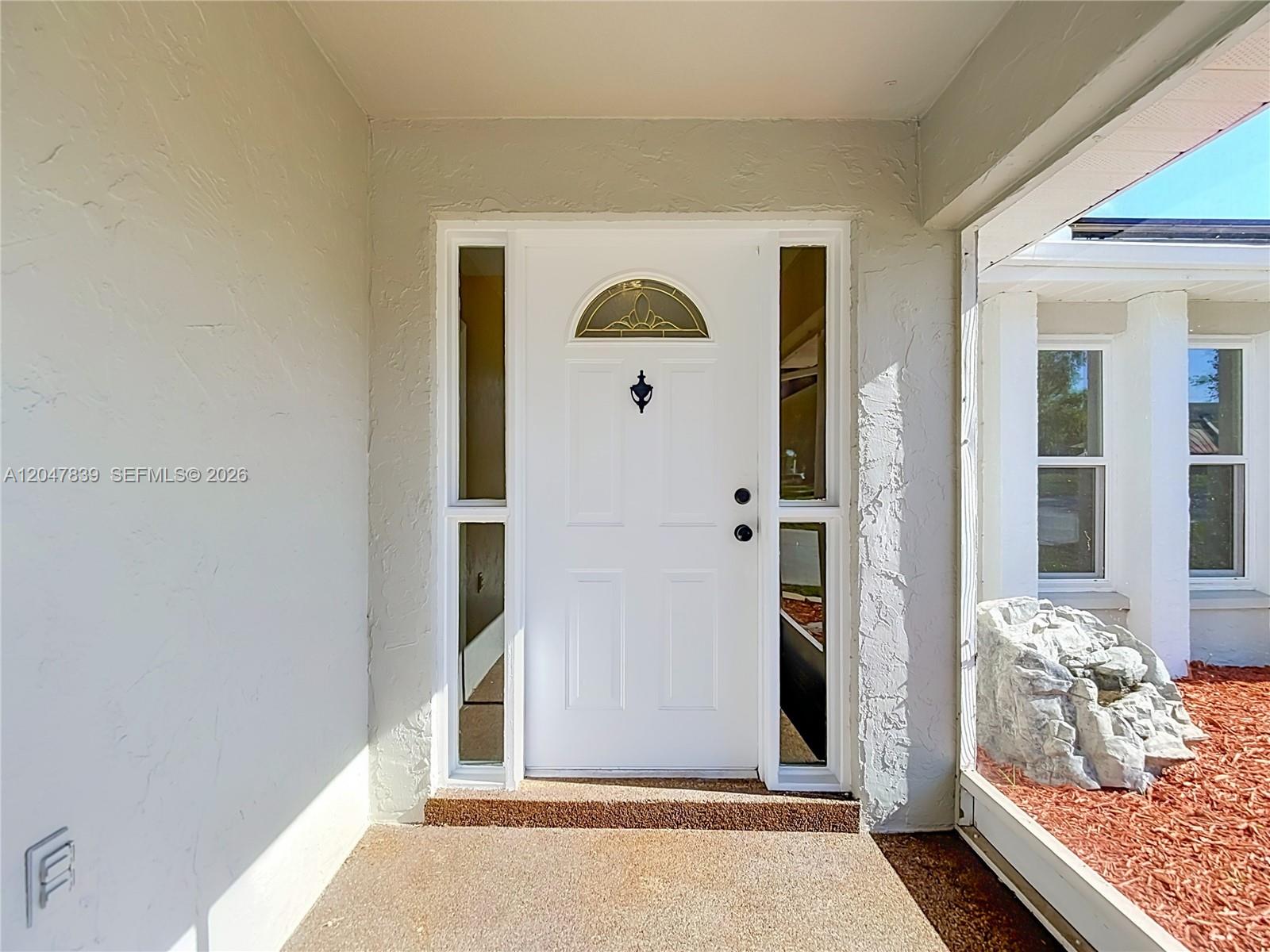 A white front door with sidelights and a decorative knocker sits under a covered entryway — 8209 Chaucer Dr, Spring Hill FL 34607, SPRING HILL, FL