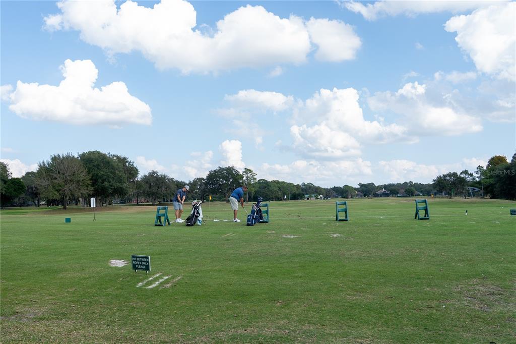 Two people practice golf on a grassy driving range under a cloudy blue sky — 552 TETON STREET, LAKE MARY, FL