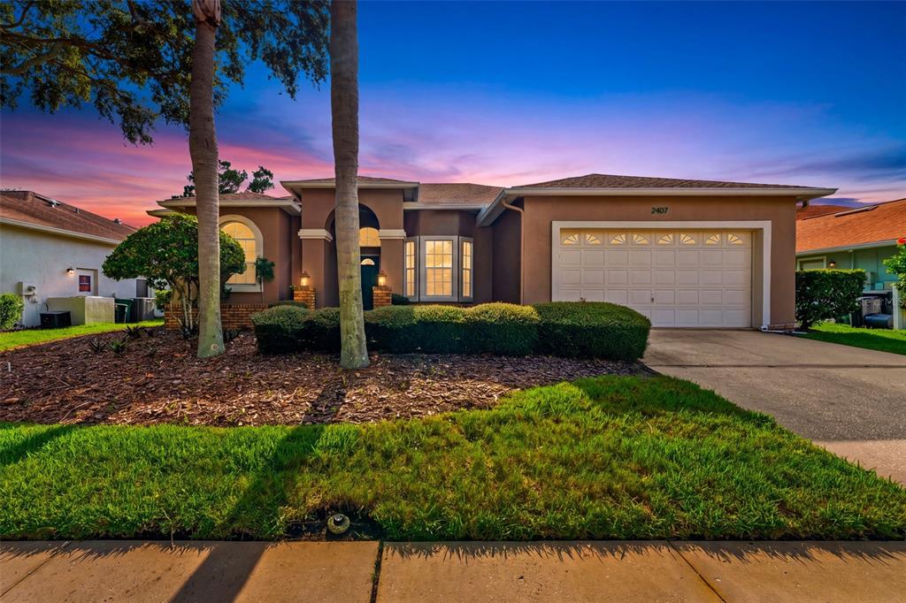 A single-story suburban house with a tan stucco exterior, a two-car garage, and palm trees — 2407 DANA DRIVE, SAFETY HARBOR, FL