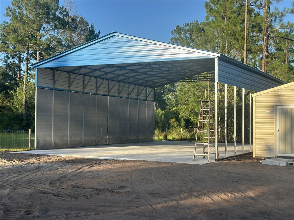 A large, open-sided metal carport structure stands on a concrete slab next to a shed — 10220 CROTTY AVENUE, HASTINGS, FL