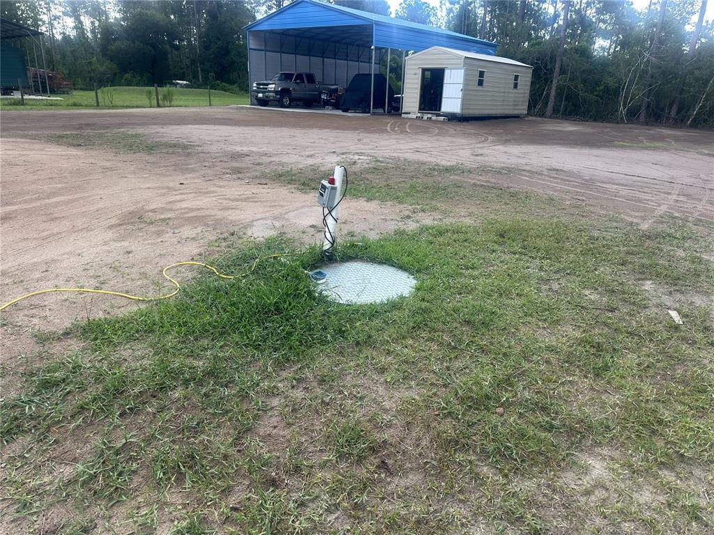 A metal well cover and electrical control box sit in a grassy yard near a carport — 10220 CROTTY AVENUE, HASTINGS, FL