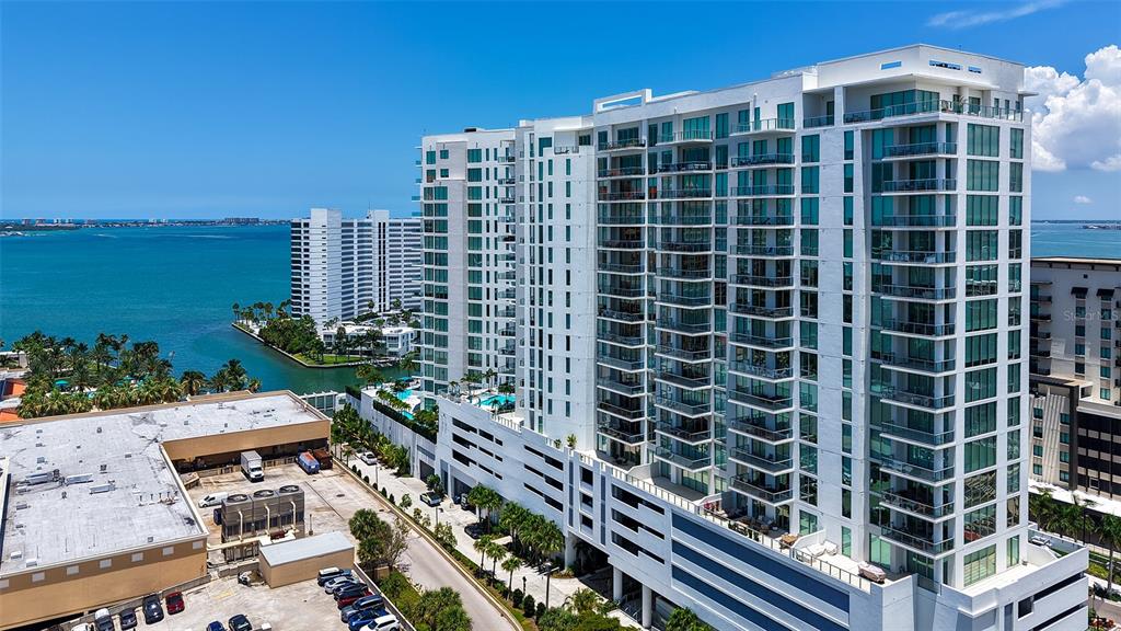 An aerial view shows a tall white residential building next to a bay and parking lot — 301 QUAY UNIT 1507, SARASOTA, FL