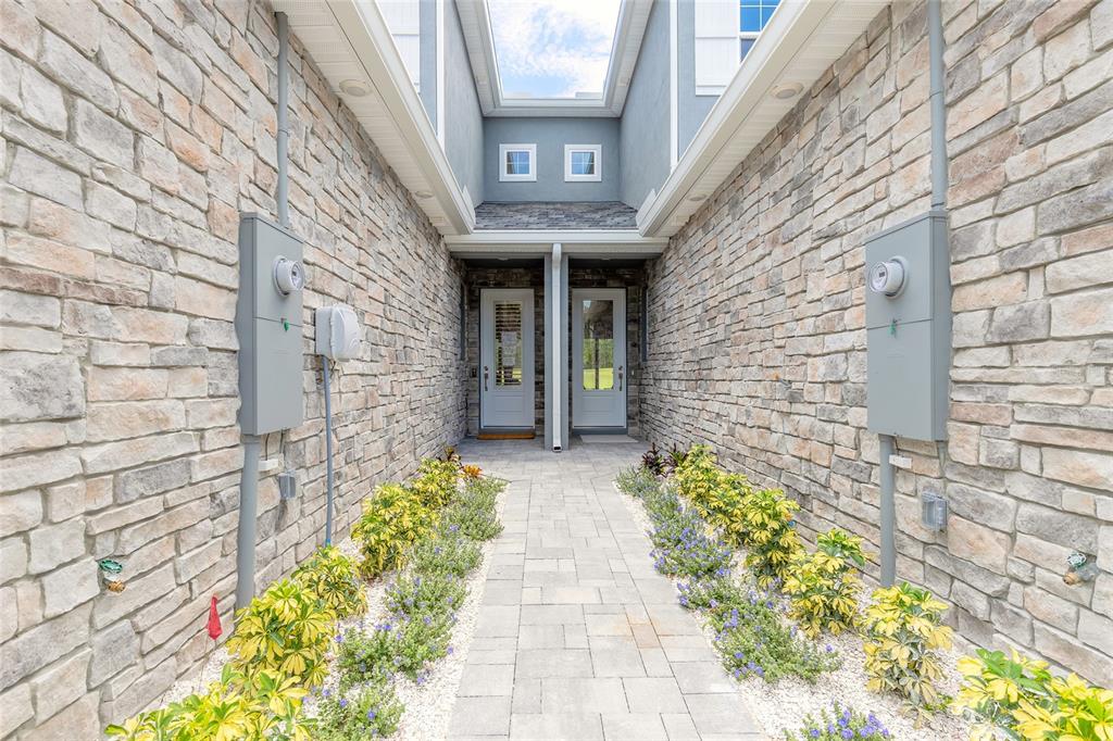 A stone-walled walkway leads to two adjacent white front doors between two residential units — 3065 ISLES WAY, NEW SMYRNA BEACH, FL
