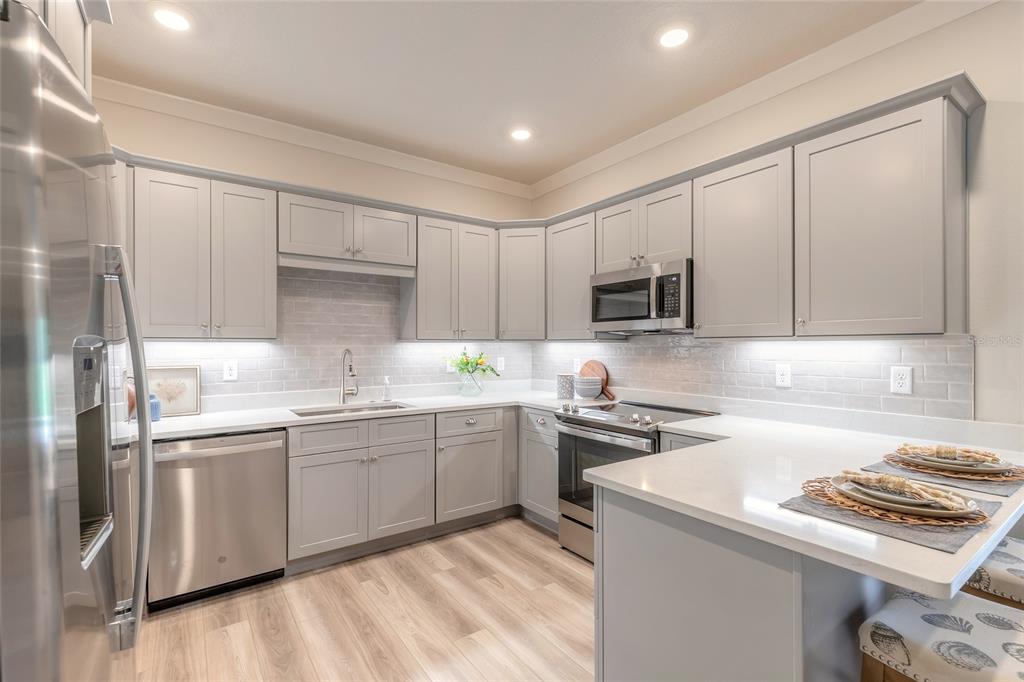 A modern kitchen features light gray cabinets, stainless steel appliances, and white quartz countertops — 3065 ISLES WAY, NEW SMYRNA BEACH, FL
