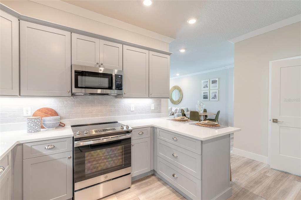 A modern kitchen features light gray cabinets, stainless steel appliances, and white countertops — 3065 ISLES WAY, NEW SMYRNA BEACH, FL