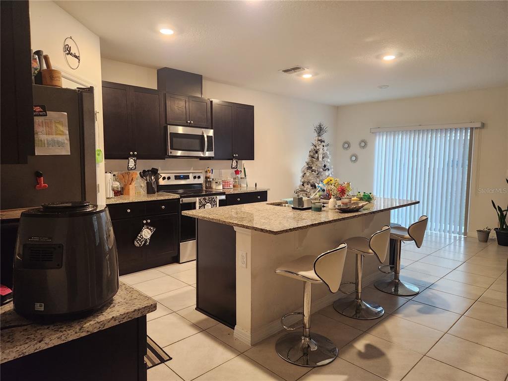 A kitchen features dark cabinets, granite countertops, a center island with bar seating, and tile flooring — 1075 GRIFFON AVENUE, LAKE ALFRED, FL