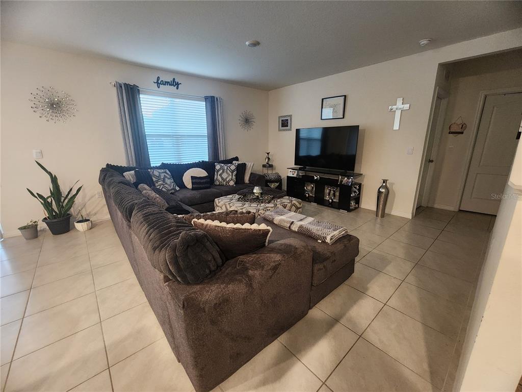 A living room features a large sectional sofa, a television on a stand, and tile flooring — 1075 GRIFFON AVENUE, LAKE ALFRED, FL