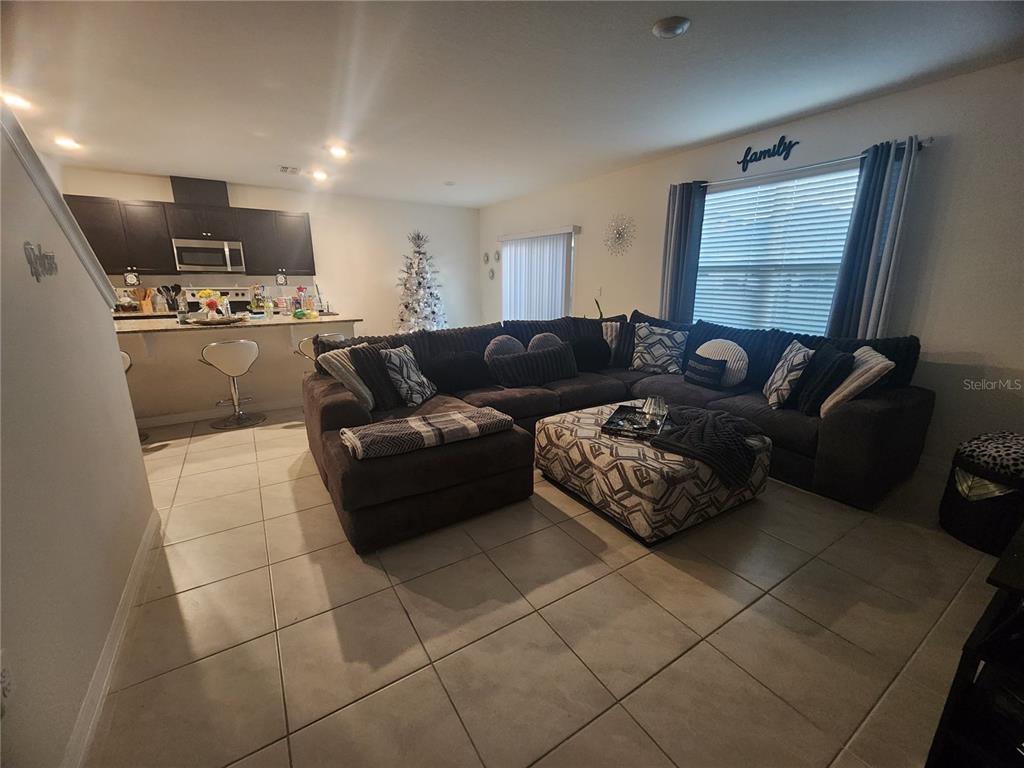 An open-concept living room features a large sectional sofa, a patterned ottoman, and a kitchen — 1075 GRIFFON AVENUE, LAKE ALFRED, FL